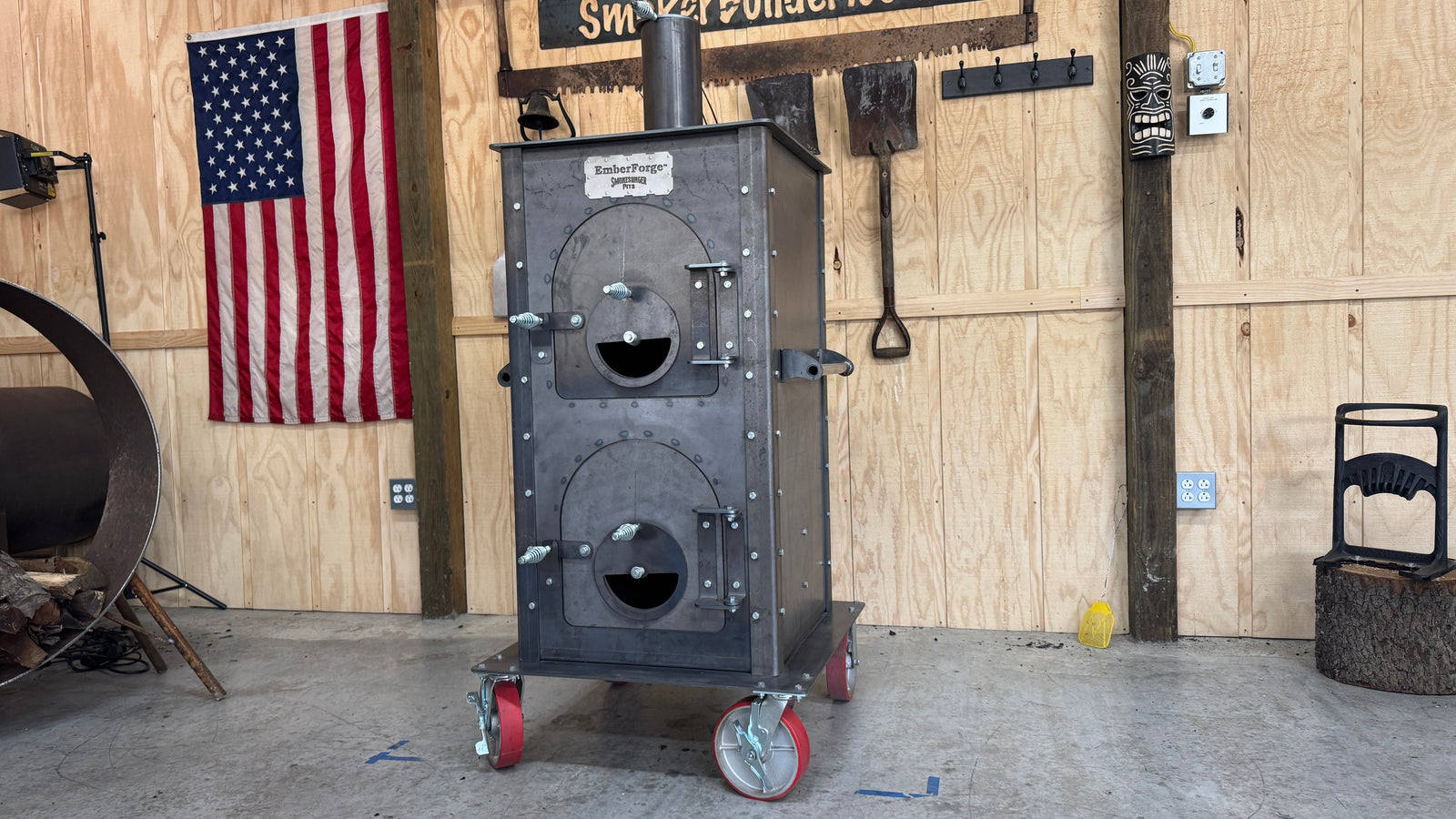 image of the emberforge in front of a wood paneled wall with some bbq tools and the American flag hanging in the back left of the image