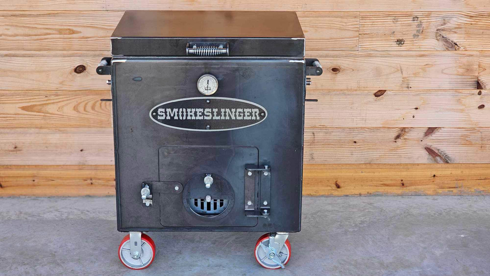 image of the top front view of a smokeslinger smoker sitting on concrete with a natural stained wood wall in the bacground