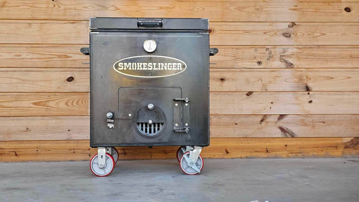 image of the front view of a smokeslinger smoker sitting on concrete with a natural stained wood wall in the bacground