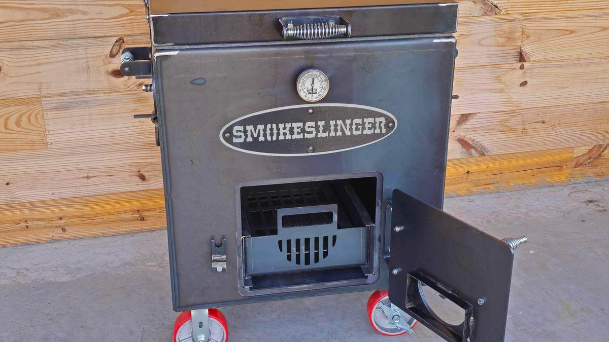 image of the top view of a smokeslinger smoker with the fire box door open sitting on conrete with a natural stained wood wall in the bacground