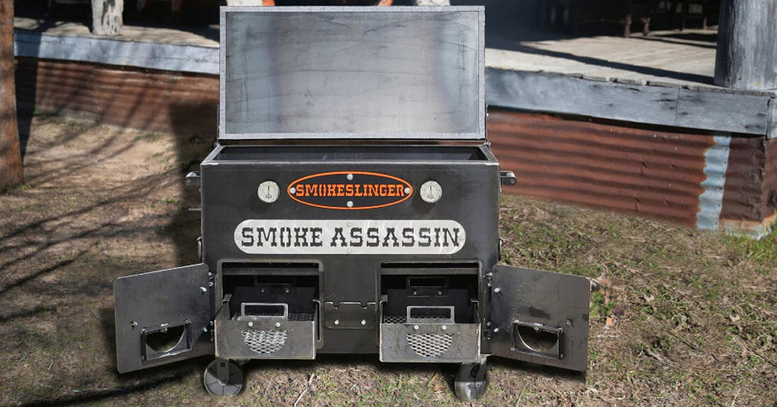image of the front view of a smokeslinger smoker sitting on grass outside a house in front of the porch in the background with all the doors open and the charcoal baskets slid out