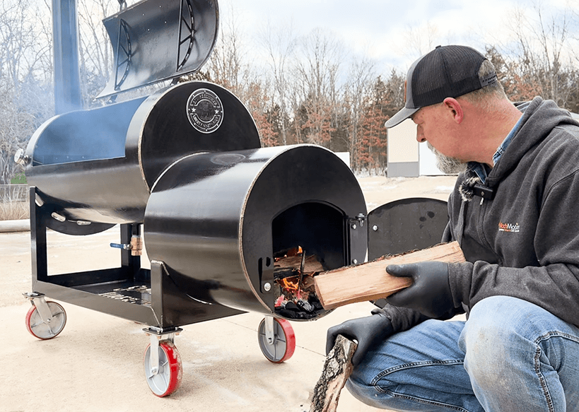 Frank Cox of smokerbuilder adding a log to the Liberty94 offset smoker fire box